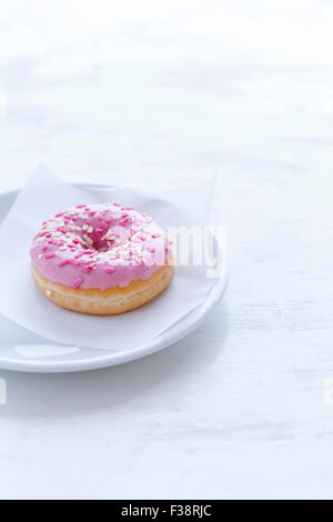 Rosa Donut, nur eine auf einem weißen Teller Stockfoto