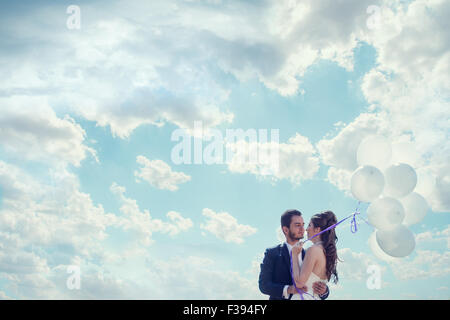Frisch verheiratete Braut und Bräutigam mit Ballons in der Hand über bewölkten Himmel. Gefühle und Liebe. Glück und Freude Stockfoto