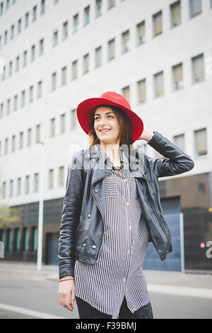 Knie-Figur des jungen schöne Brünette asiatische Mädchen gehen in den Vororten mit Blick auf recht gekleidet mit roten Hut, schwarze Jeans und schwarzen und weißen Streifenhemd - Sorglosigkeit, Jugendkonzept Stockfoto