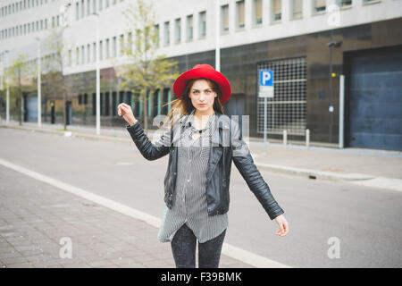 Knie-Figur des jungen schöne Brünette asiatische Mädchen gehen in den Vororten mit Blick auf recht gekleidet mit roten Hut, schwarze Jeans und schwarzen und weißen Streifenhemd - Sorglosigkeit, Jugendkonzept Stockfoto