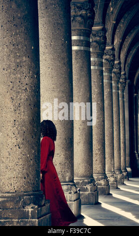 Geheimnisvolle Frau im roten Kleid hinter Spalte Stockfoto