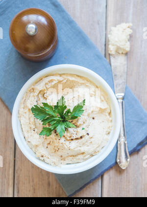 Hummus (Hummus) Sprung in eine weiße Schüssel mit Petersilie, auf einem hölzernen Hintergrund dekoriert. Stockfoto