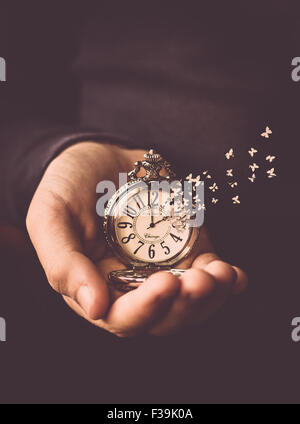 Mann, der eine Uhr mit der Zeit aus dem Zifferblatt wie Schmetterlinge fliegen in seiner Hand hält Stockfoto