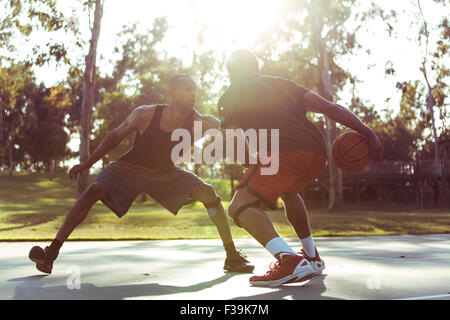 Zwei junge Männer spielen Basketball im Park bei Sonnenuntergang Stockfoto