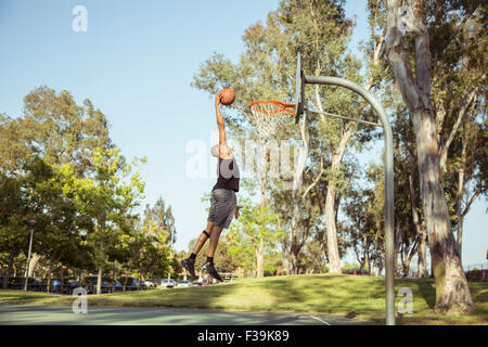 Mann schießen Basketballkörbe im Park bei Sonnenuntergang Stockfoto
