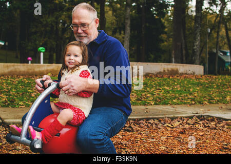 Mädchen spielen mit ihrem Großvater auf dem Spielplatz Stockfoto