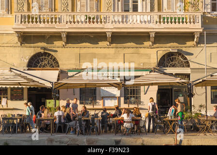 Trieste Café, Blick bei Sonnenuntergang von Touristen entspannen auf einer Café-Terrasse am Canal Grande in Triest, Italien. Stockfoto