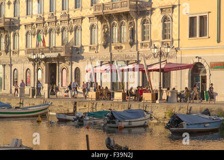 Triester Sommer, Blick auf einen Sommernachmittag mit Menschen, die sich an Cafétischen auf einer Terrasse am Canal Grande in Triest, Italien, entspannen. Stockfoto