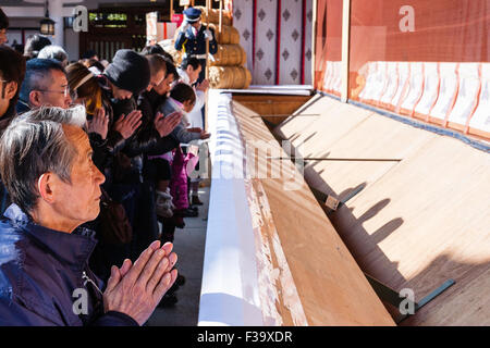 Japan, neues Jahr, Winter. Japanische älterer Mann, zusammen halten sich an den Händen und Beten beim Stehen vor der Saisen an überfüllten Shinto Schrein. Tagsüber. Stockfoto