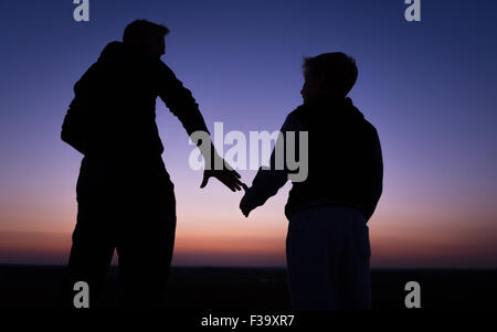 Förderung und Erziehung Konzept Foto von Vater und Sohn in der Silhouette, die Hand in Hand, den Sonnenuntergang beobachten Stockfoto