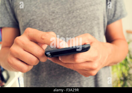Closeup von einem kaukasischen Jüngling in einem grauen T-shirt mit einem Smartphone im Innenbereich Stockfoto