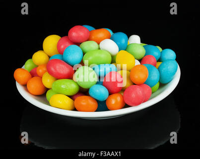 bunte Bonbons in weiße Untertasse auf schwarzem Hintergrund isoliert Stockfoto