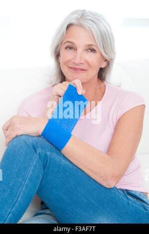 -MODELL VERÖFFENTLICHT. Reife Frau setzen einen Verband an ihrem Handgelenk. Stockfoto