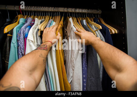 Mann auf der Suche nach ein Hemd auf der Schiene in seine Garderobe, erste Personenansicht nach unten seine Arme hängen. Selbst POV Stockfoto