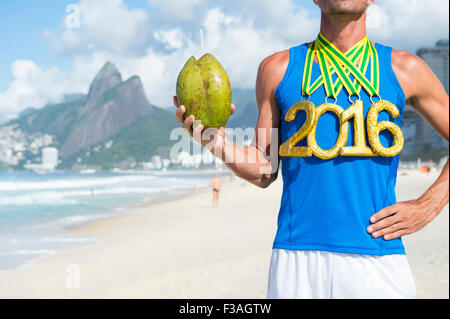 Goldmedaille 2016 Sportler halten frische Coco Gelado grüne Kokosnuss am Strand von Ipanema in Rio De Janeiro, Brasilien Stockfoto