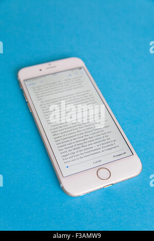 Lesen Sie ein Ebook auf eine goldene und weiße Apple iPhone 6 Againdt einen blauen Hintergrund Stockfoto