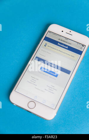 Gold und weiße Apple iPhone 6 mit einem Facebook anmelden Bildschirm vor einem blauen Hintergrund Stockfoto