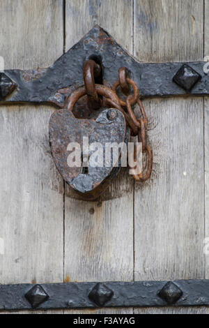 alte rostige Vorhängeschloss und Kette auf Schmiedeeisen und Holztür Stockfoto