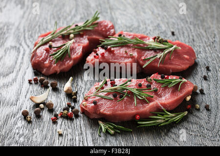 Drei saftige rohes Rindfleisch Steaks garniert mit Zweigen Rosmarin, Knoblauch und Pfefferkörner Stockfoto