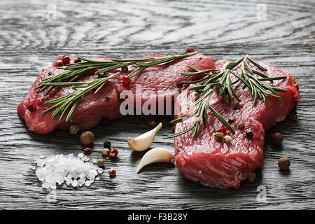 Ein paar saftige rohes Rindfleisch Steaks garniert mit Zweigen Rosmarin, Knoblauch und Pfefferkörner Stockfoto