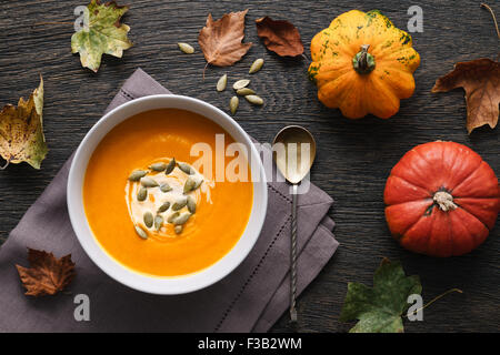 Traditionelle Kürbissuppe auf dunklem Holz Hintergrund mit Herbstlaub und dekorative Kürbisse. Stockfoto