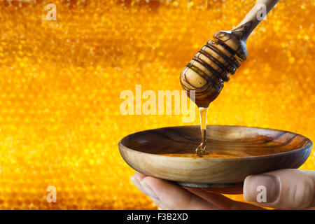 Eine Frau Hand mit einer hölzernen Abschlag Schüssel mit einem Schöpflöffel und Honig auf Waben Hintergrund. Stockfoto