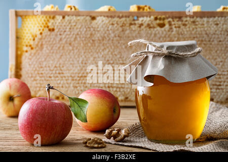 Glasdose voller Honig mit frischen Äpfeln und Walnüssen auf den Waben-Hintergrund. Stockfoto