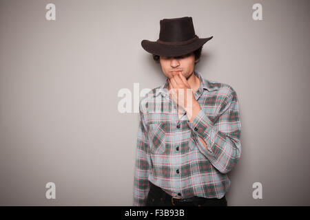 Ein junger Cowboy trägt ein kariertes Hemd posiert vor einer grünen Wand Stockfoto