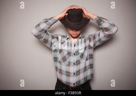 Ein junger Mann trägt einen Cowboyhut und ein kariertes Hemd posiert vor einer grünen Wand Stockfoto