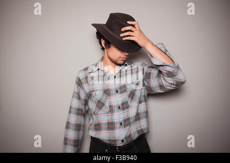 Ein junger Mann trägt einen Cowboyhut und ein kariertes Hemd posiert vor einer grünen Wand Stockfoto
