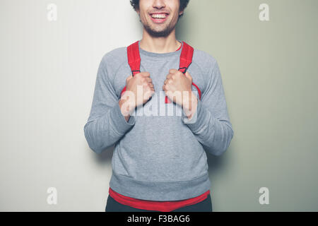 Junge Mann trägt einen roten Rucksack steht vor einem grünen und weißen Hintergrund Stockfoto