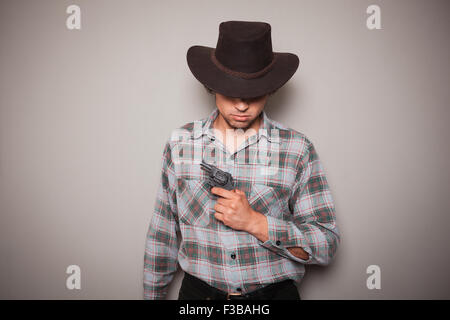 Ein junger Mann trägt einen Cowboyhut und ein kariertes Hemd hält einen revolver Stockfoto
