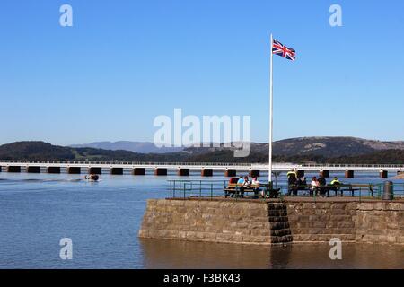 Flagge auf Arnside Pier bei Flut mit Arnside Eisenbahnviadukt über die Mündung des Flusses Kent hinter dem Pier. Stockfoto