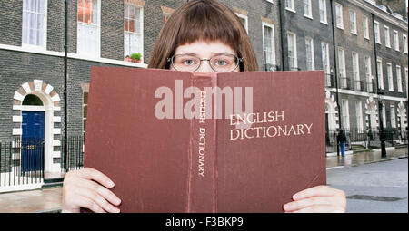 Mädchen mit Brille blickt auf English Dictionary Buch und London Street auf Hintergrund Stockfoto