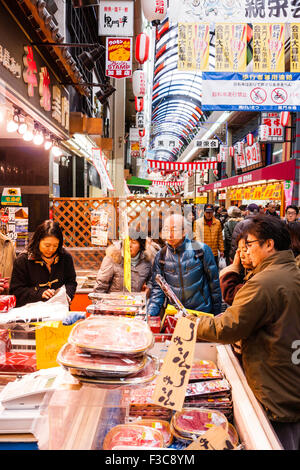 Besetzt fish monger stall Verkauf vorverpackte Meeresfrüchte an: Kuromon Ichiba Lebensmittelmarkt kurz vor dem Neuen Jahr in Osaka. Die Leute, die auf der Suche und Auswahl von Paketen. Stockfoto