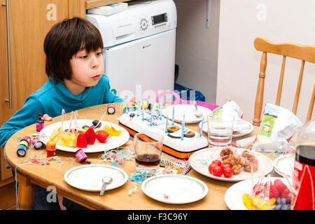 Gemischter ethnischer Zugehörigkeit, (Japanisch, Englisch) 11 Jahre alter Junge am Kopf des Küchentisch sitzen Kerzen ausblasen auf Geburtstagskuchen. Andere Lebensmittel und Getränke. Stockfoto