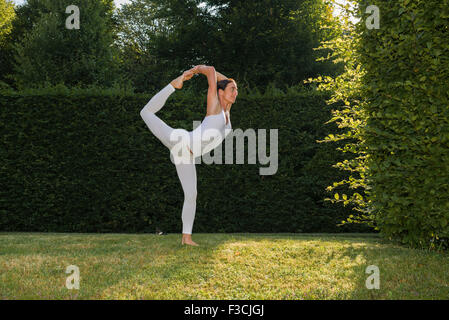 Junge Frau, eine weiße Babybody, übt Hatha-yoga im Freien zwischen Bäumen, die Pose: natarajasana, Herrn Shi Stockfoto