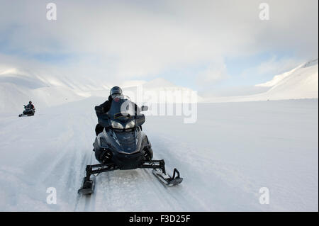 Mann mit Motorschlitten auf dem Weg in einer verschneiten Landschaft mit Gletscher hinter Semmeldalen, Spitzbergen, Svalbard, Norwegen. Stockfoto