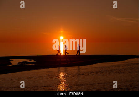 Silhouetten von eine nicht identifizierte Personen zu Fuß am Strand bei Sonnenuntergang mit den Sonnenuntergang als Hintergrund Stockfoto