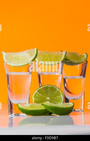 Tequila shot mit einer Scheibe Limette auf dem Glas auf orangem Hintergrund. Selektiven Fokus Stockfoto