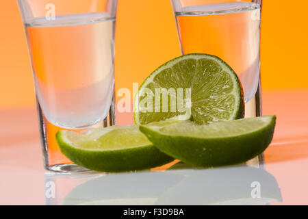 Tequila shot mit einer Scheibe Limette auf dem Glas auf orangem Hintergrund. Selektiven Fokus Stockfoto