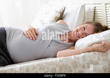 Schwangere Frau auf Bett liegend lächelnd Stockfoto