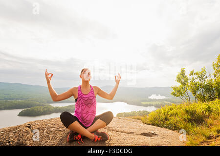 Junge Frau im Lotussitz gegen See Stockfoto