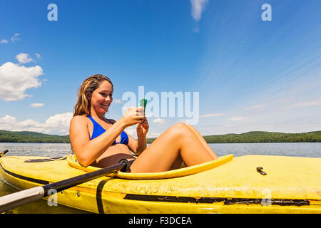 Junge Frau mit Smartphone im Kajak auf See Stockfoto
