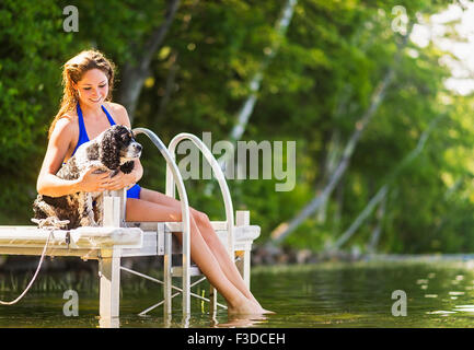 Junge Frau mit Hund sitzt am Hafenkai auf See Stockfoto