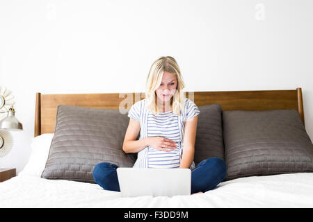 Schwangere Frau mit Laptop im Bett Stockfoto