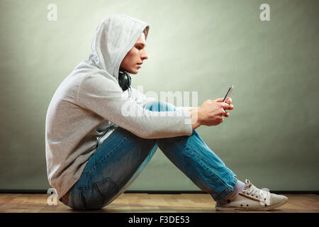 Junge Menschen und Freizeit-Konzept. vermummte Mann teenboy mit Kopfhörern am Boden hören Musik Grunge Hintergrund Stockfoto