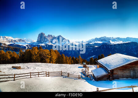 Alphütte, umgeben von einem Zaun im Schnee vor dem Panorama der schneebedeckten Gipfeln an einem sonnigen Tag im Winter auf Dolomiten Alpen Stockfoto