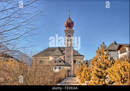 Der Luis Trenker Promenade führt bis St. Ulrich, italienisches Dorf in Dolomiten Alpen: typische Häuser, Gebäude und die roten Glockenturm mit Uhr Pfarrkirche St. Ulrich mit Bergen und grünen Koniferen im Hintergrund Stockfoto