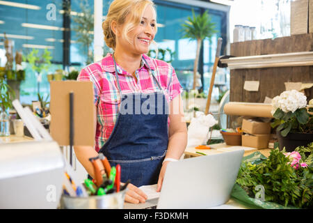 Lächelnd mit Laptop am Schalter im Blumenladen Blumengeschäft Stockfoto